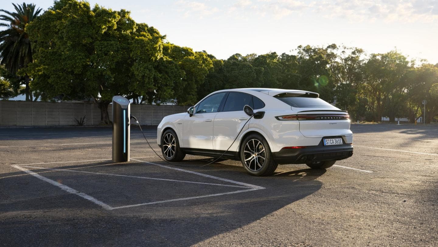Weißer Porsche Cayenne E-Hybrid Coupé an einer Ladesäule auf einem sonnigen Parkplatz