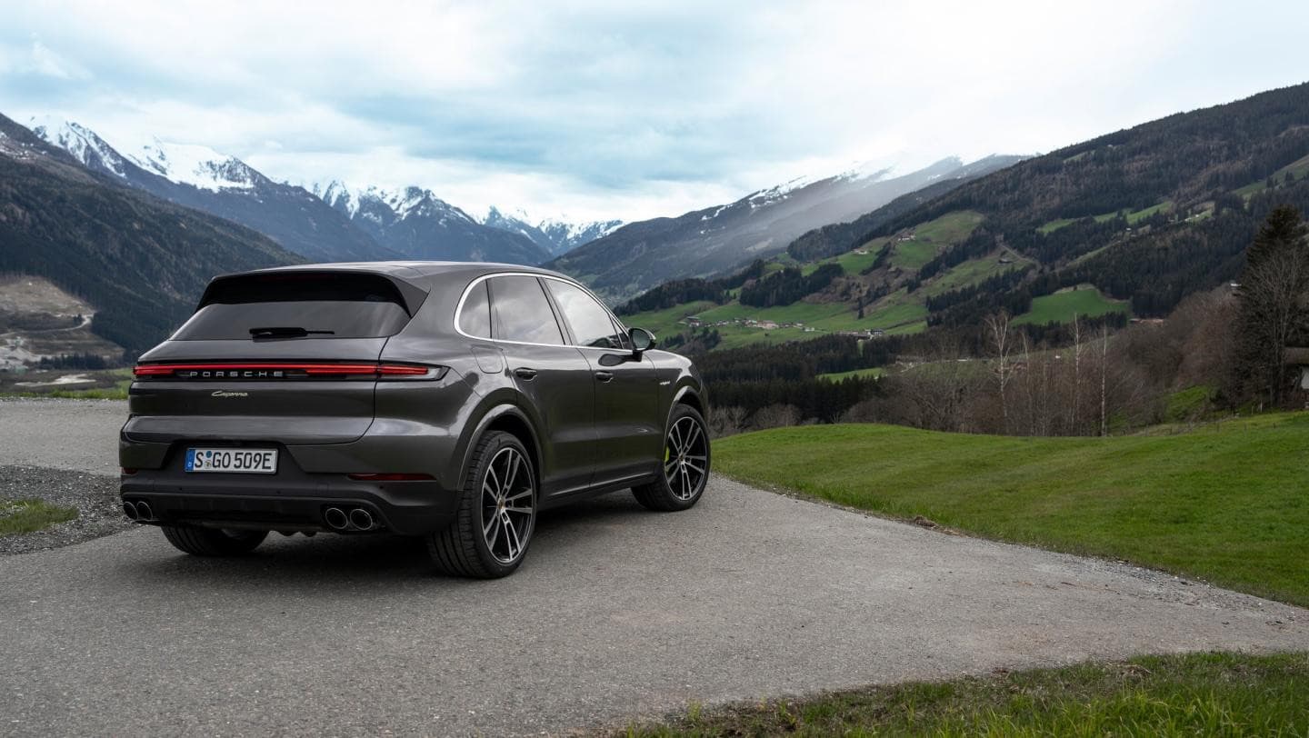 Grauer Porsche Cayenne E-Hybrid schräg von hinten vor einem Bergtal